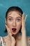 Close-up portrait of surprised young fashion model with cherry berry. Freckled girl bites cherry in front of blue background