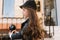 Close-up portrait of thoughtful long-haired kid standing in front of cafe and holding iron pillar. Charming little curly