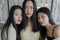 Close up portrait of three beautiful young Asian female friends casually pose for the camera together inside a rustic room, young