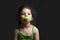 Close-up portrait of a three years old girl with pacifier and green stirrup in front of dark background