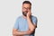 Close up portrait of tired calm man standing isolated over white background, looking directly at camera, touching his face with