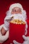 Close-up portrait Traditional Santa Claus watching TV, eating popcorn. Christmas. Red background. emotions. fear