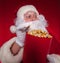 Close-up portrait Traditional Santa Claus watching TV, eating popcorn. Christmas. Red background. emotions. fear