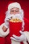 Close-up portrait Traditional Santa Claus watching TV, eating popcorn. Christmas. Red background. emotions. fear