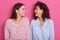 Close up portrait of two beautiful young women posing over pink background, friends wearing casually clothing, standing and look