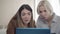 Close-up portrait of two focused young women using laptop indoors. Concentrated beautiful blond and brunette colleagues