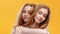 Close up portrait of two hugging young redhaired twin sisters, enjoying their connection, orange studio background