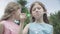 Close-up portrait of two identical twin sisters blowing soap bubbles outdoors on summer day. Cute brunette Caucasian