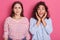 Close up portrait of two stupefied young women standing closely to each other, stare with bugged eyes, being shocked by sudden