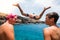 Close up and portrait of two teenagers talkinng together smiling and laughing at the beach while another man is jumping on their