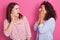 Close up portrait of two women look at each other while posing isolated over pink background, hear unbelievable headlines news,