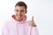 Close-up portrait of upbeat smiling, satisfied blond male student in pink hoodie, looking satisfied show thumb-up in