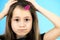 Close up portrait of upset and pensive little girl with cute pink hairpin on blue background