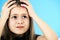 Close up portrait of upset and pensive little girl with cute pink hairpin on blue background