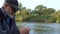 Close up portrait view of an old fisherman in a cap and glasses and with a cigarette in his mouth angling with a rod in