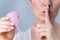 Close-up portrait of a woman holding a pink menstrual cup on a white background. Girl holding index finger to her mouth