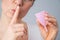 Close-up portrait of a woman holding a pink menstrual cup on a white background. Girl holding index finger to her mouth