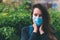 Close-up portrait of woman in protective medical mask on her face, holding hands near the face, surprised outdoor.