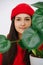 Close up portrait of a woman in vibrant red cap behind monstera leaves