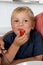 Close up portrait of young 3 years old boy with his mother at home kitchen eating fruit or tomato enjoying happy in healthy nutrit