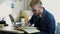 Close up portrait of young attractive man with glasses and yellow hair makes notes on diary. Home freelancer woring on