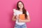 Close up portrait of young attractive woman holding her notebook isolated over rosy background, looks smiling directly at camera,