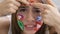 Close-up portrait of young attractive woman with painted social media icons on her face looking at camera touching her