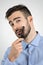 Close up portrait of young bearded man combing his beard looking at camera.