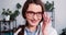 Close-up portrait of young beautiful Caucasian female doctor wear lab coat, eyeglasses posing at light clinic office.