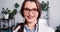 Close-up portrait of young beautiful Caucasian female doctor wear lab coat, eyeglasses posing at light clinic office.