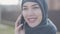Close up portrait of a young beautiful muslim woman in black headdress talking by cell phone close up. Cute asian girl