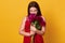 Close up portrait of young brunette woman holding bouquet of maroon peonies, posing isolated over yellow studio background,