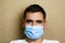 Close-up portrait of young caucasian brown-haired man in blue medical mask at home looking at camera. Lifestyle. Handsome guy.