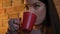 Close-up portrait of young caucasian girl with red cup enjoying the hot drink on cosy home background.