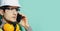 Close-up portrait of young construction wearing safety equipment and talking on smartphone. Background of aqua menthe color.