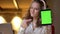 Close-up portrait of young curly-haired businesswoman watching into tablet and showing its green screen to camera.