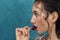 Close-up portrait of young fashion model with cherry berry. Freckled girl touches lips with cherry in front of blue background