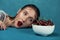 Close-up portrait of young fashion model with plate of cherry berry. Freckled girl bites cherry in front of blue background