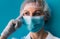 Close-up portrait of young female doctor in medical cap, mask, white gown and gloves on blue background. D