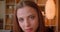 Close-up portrait of young female student watches into camera attentively and smiles on bookshelves background.