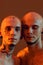 Close up portrait of young half naked twin brothers with tattoos and piercings posing together isolated over orange