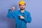 Close up portrait of young handsome manual worker holding wrench tool in hand and pointing at his stong biceps isolated over blue