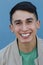 Close up portrait of a young hispanic teenager man looking at camera with a joyful smiling expression, against a blue background