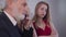 Close-up portrait of young irritated caucasian woman in red dress waiting for busy senior man talking on the phone at