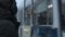 Close-up Portrait of a young long-haired man with a beard in headphones standing at a tram stop in winter and waiting