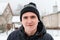 Close-up portrait of young man in warm hat outside on rural winter snowy house background. Happy millennial smiling