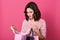 Close up portrait of young upset lady standing in studio and looking in opened shopping bag in her hands with sad facial