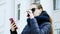 Close-up portrait of a young woman in the glasses drinking coffee using smart phone in the city