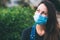 Close-up portrait of young woman in protective medical mask on her face, looking at camera outdoor.