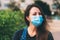 Close-up portrait of young woman in protective medical mask on her face, looking at camera outdoor.